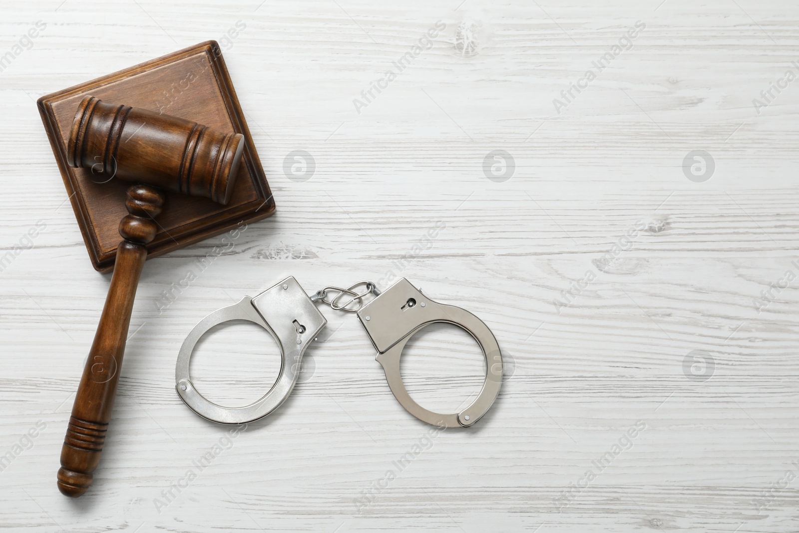 Photo of Handcuffs and judge's gavel on white wooden table, flat lay. Space for text