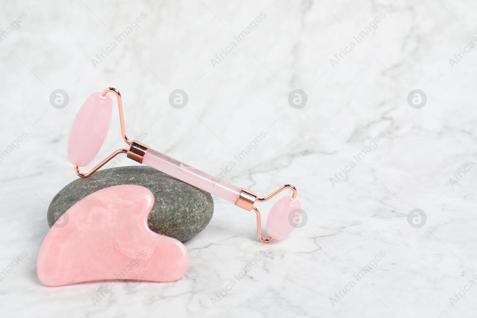 Photo of Face roller, gua sha tool and stone on white marble background. Space for text