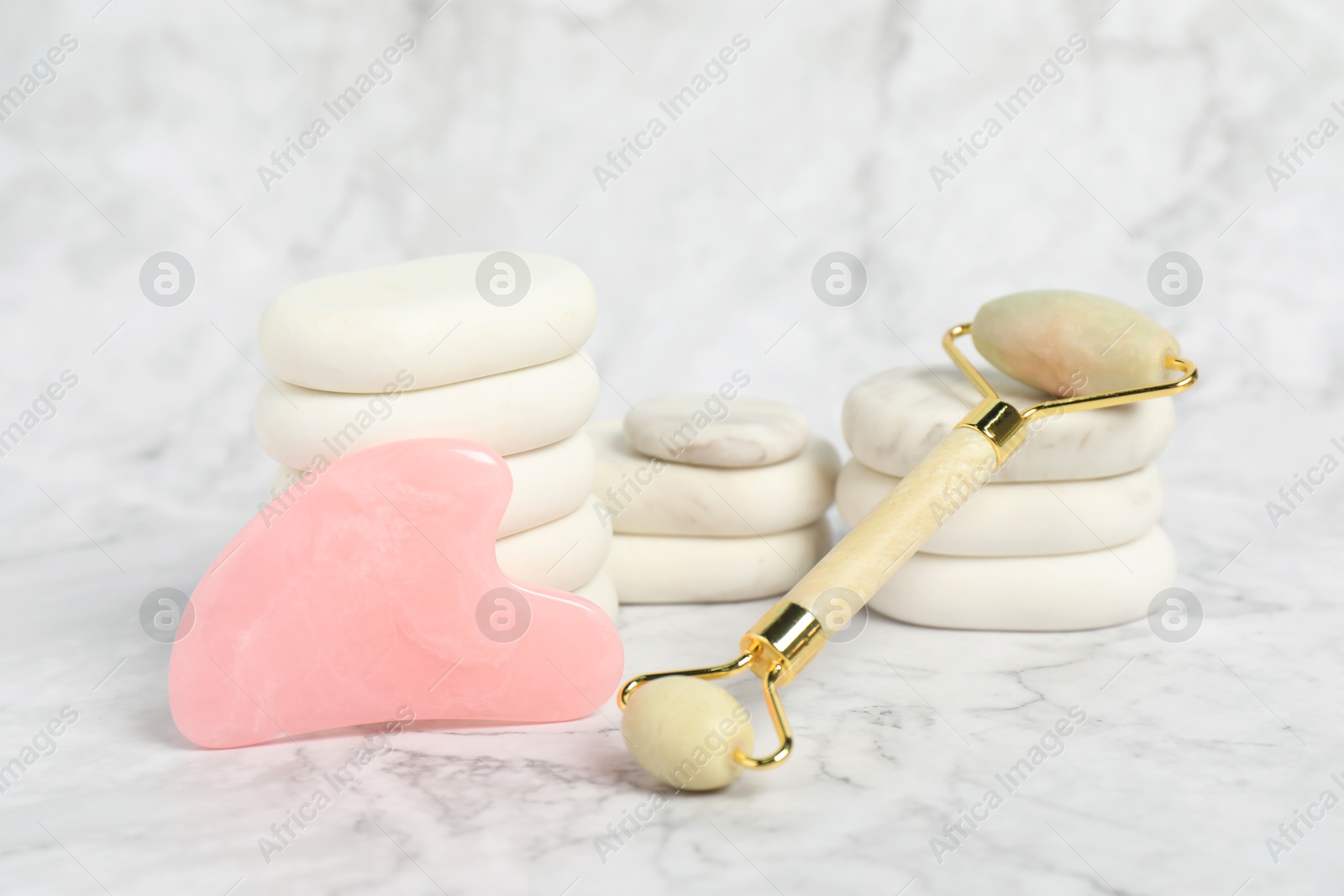 Photo of Face roller, gua sha tool and massage stones on white marble background