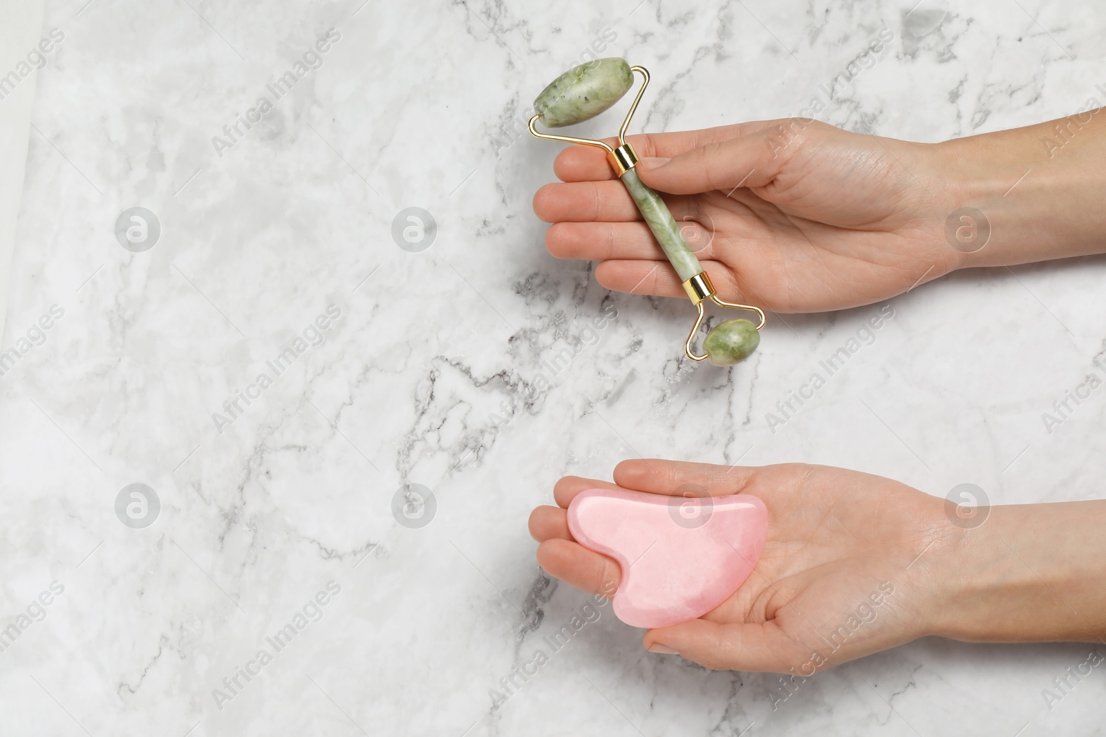 Photo of Woman with face roller and gua sha tool on white marble background, above view. Space for text