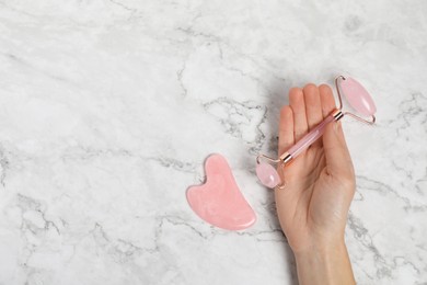 Photo of Woman with face roller and gua sha tool on white marble background, top view. Space for text