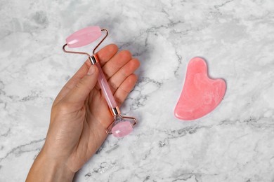 Photo of Woman with face roller and gua sha tool on white marble background, top view