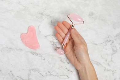 Photo of Woman with face roller and gua sha tool on white marble background, top view