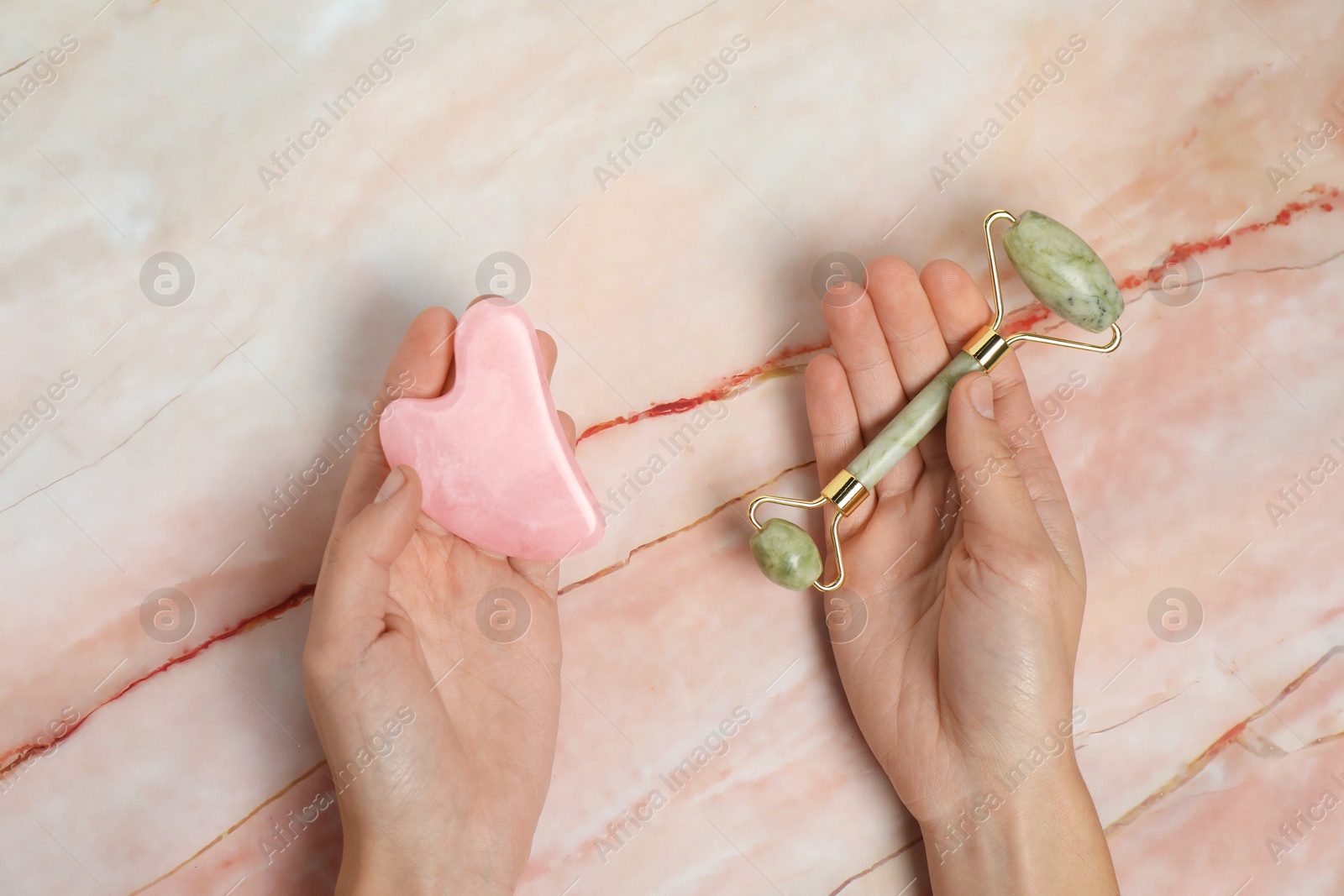 Photo of Woman with face roller and gua sha tool on pink marble background, top view