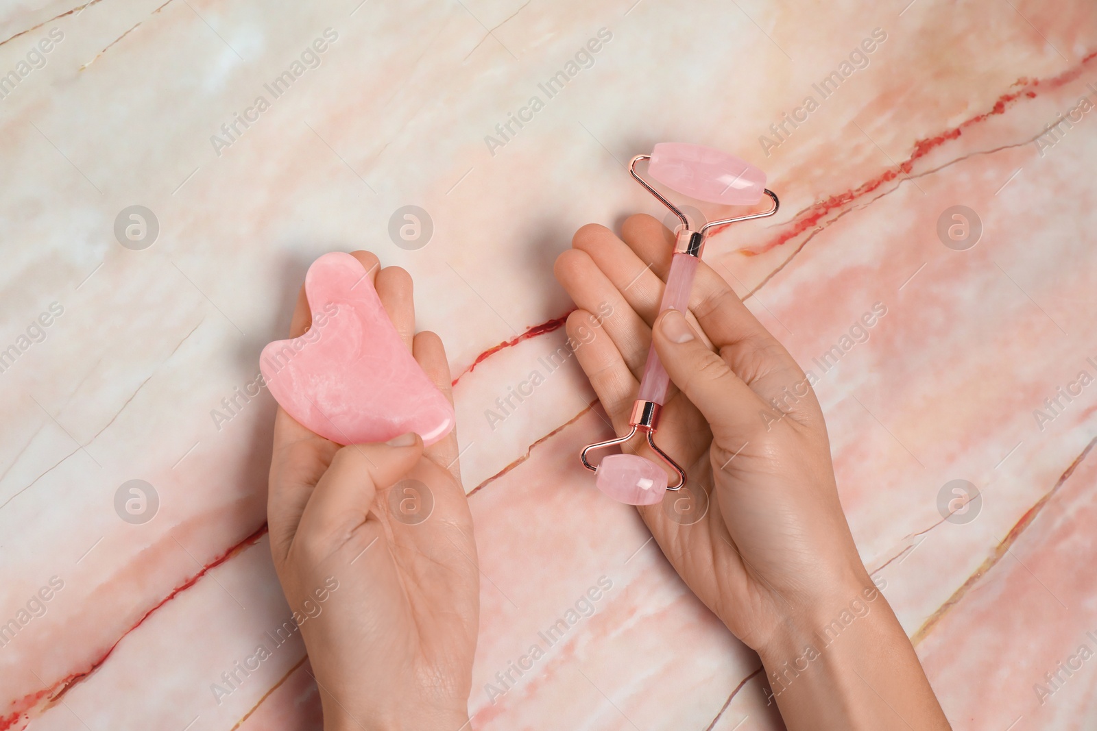 Photo of Woman with face roller and gua sha tool on pink marble background, above view