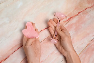 Photo of Woman with face roller and gua sha tool on pink marble background, above view