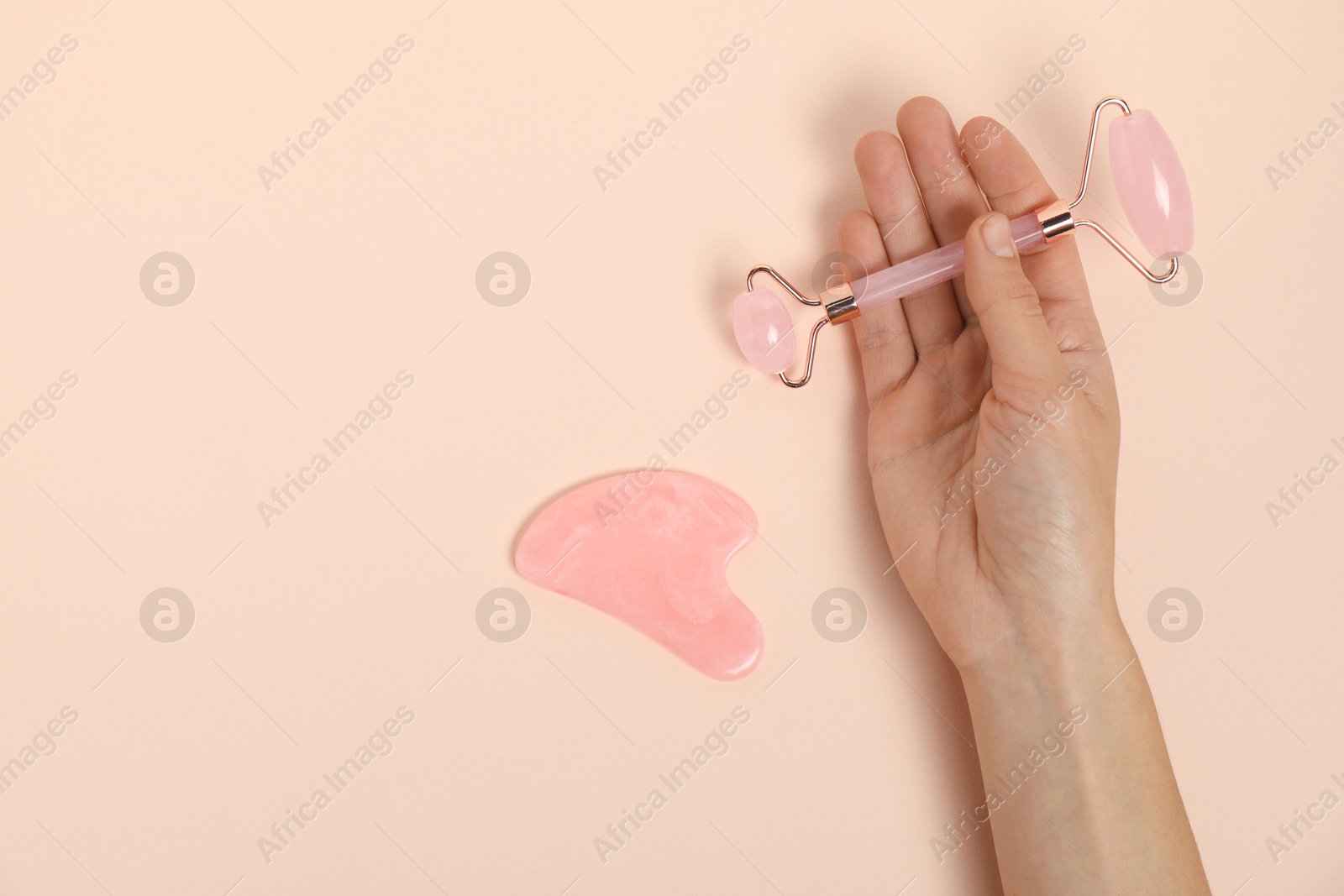 Photo of Woman with face roller and gua sha tool on beige background, top view. Space for text