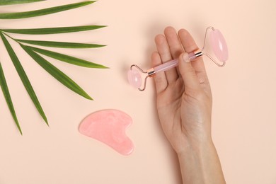 Photo of Woman with face roller, gua sha tool and leaf on beige background, top view