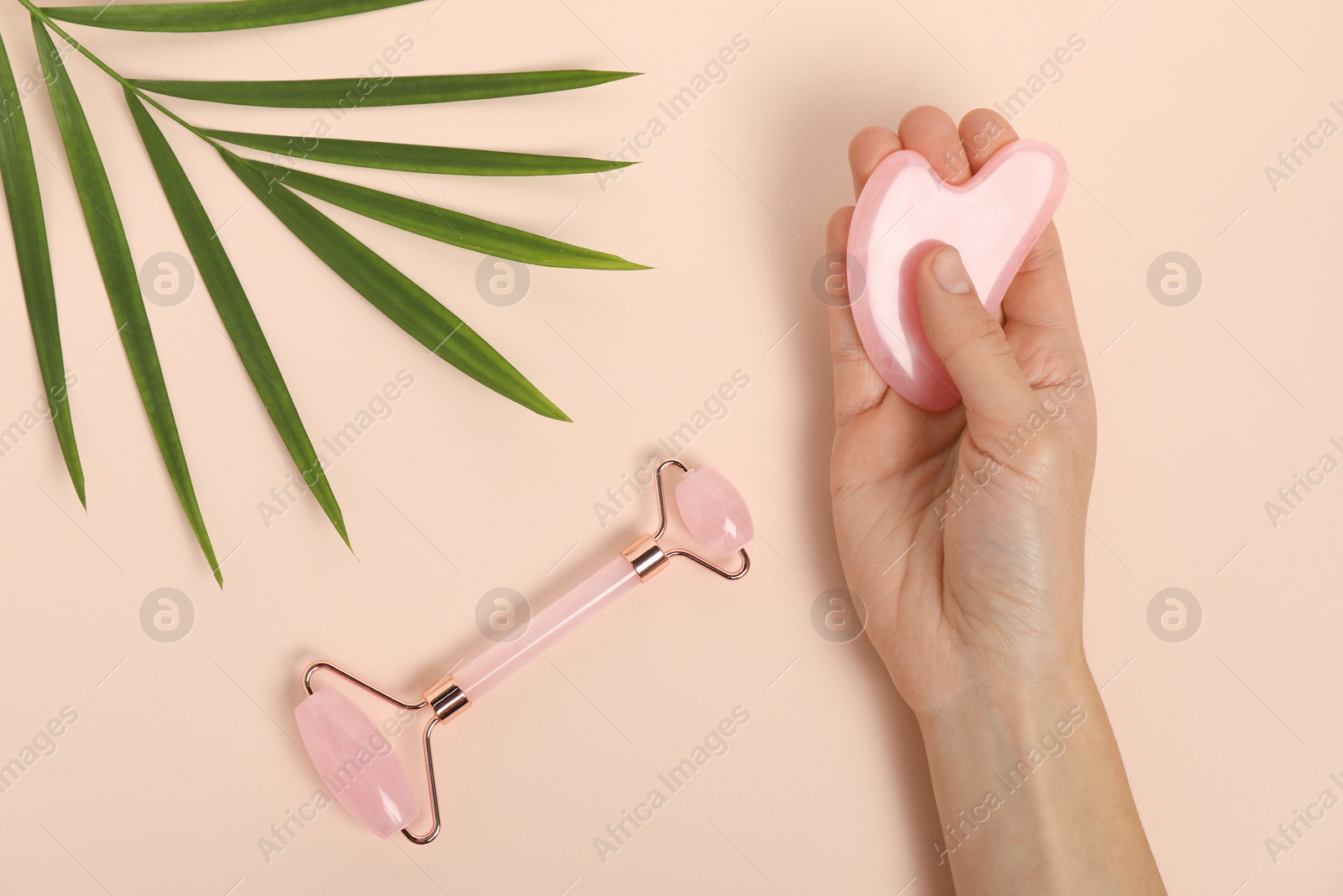 Photo of Woman with gua sha tool, face roller and leaf on beige background, top view