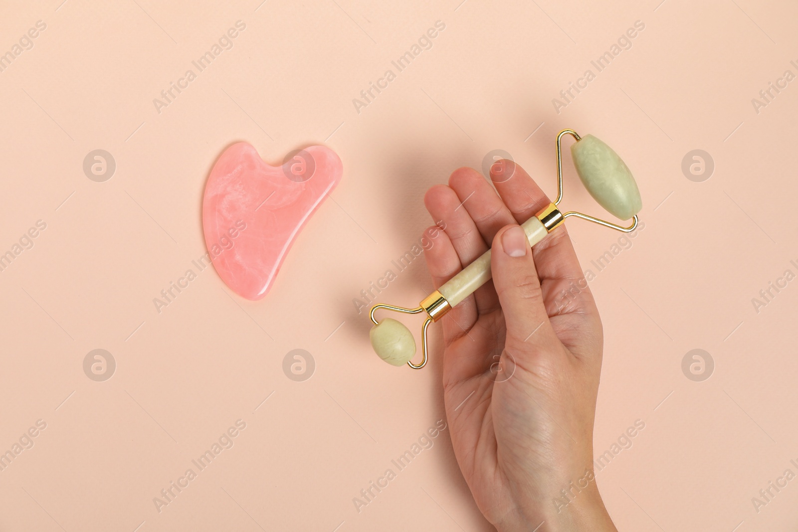 Photo of Woman with face roller and gua sha tool on beige background, top view