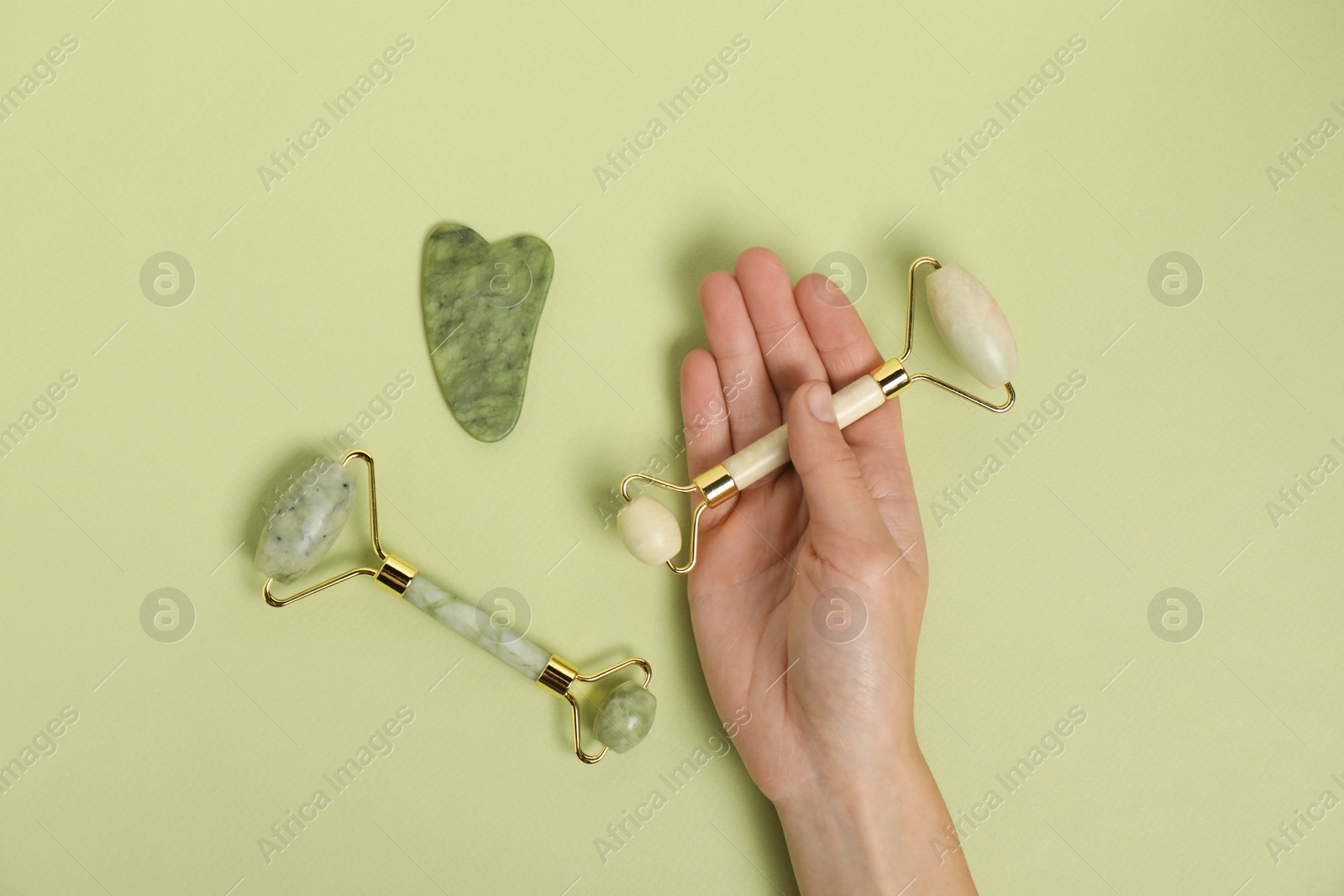 Photo of Woman with face rollers and gua sha tool on light green background, top view