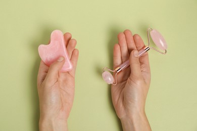 Photo of Woman with face roller and gua sha tool on light green background, top view