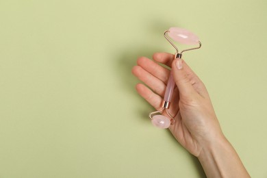 Photo of Woman with face roller on light green background, top view. Space for text