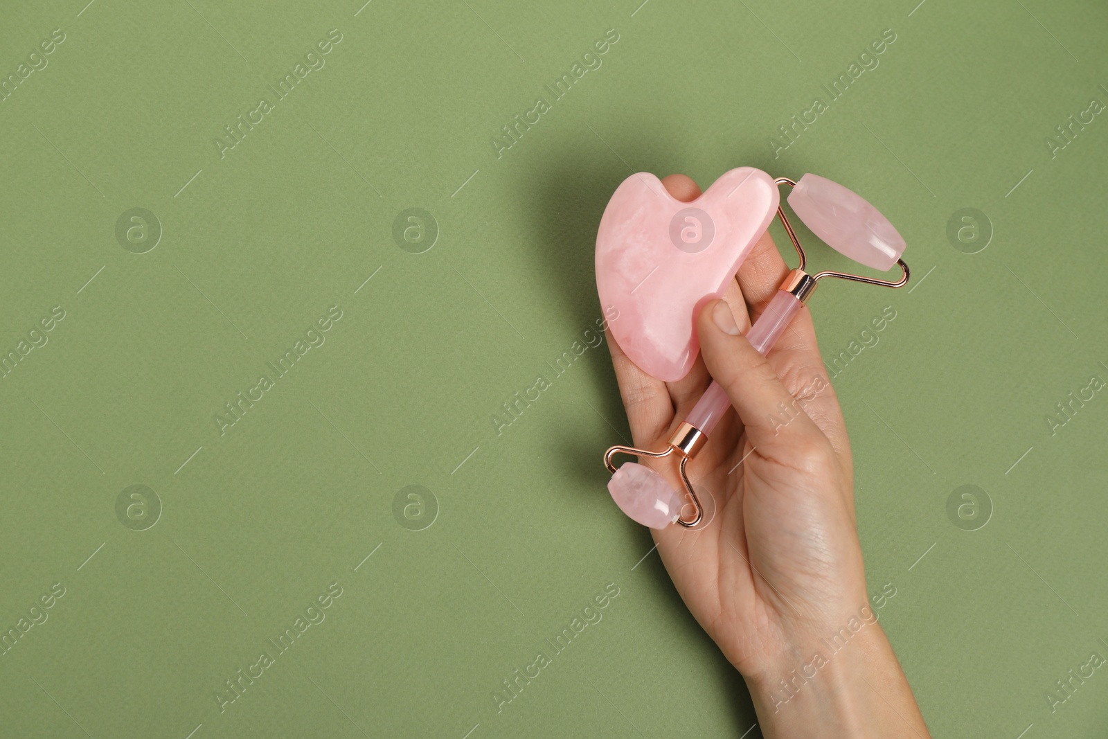 Photo of Woman with face roller and gua sha tool on green background, top view. Space for text