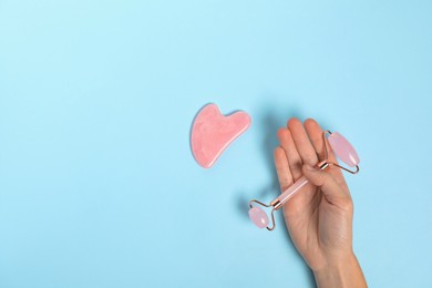 Photo of Woman with face roller and gua sha tool on light blue background, top view. Space for text