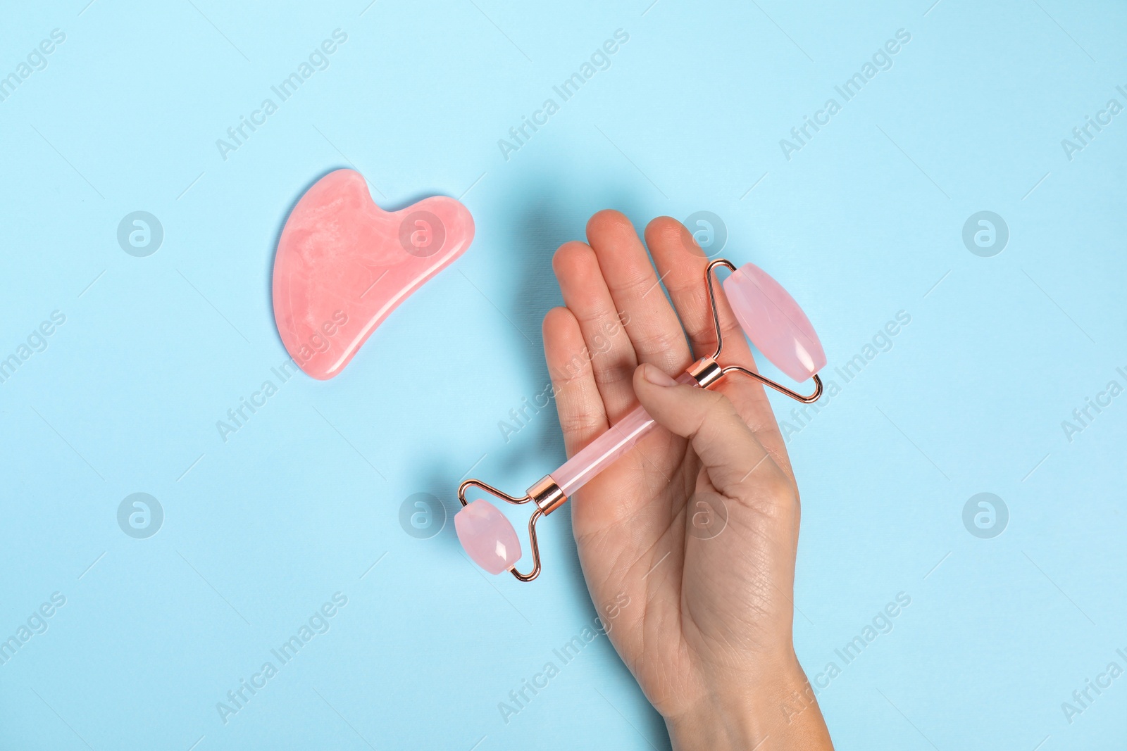 Photo of Woman with face roller and gua sha tool on light blue background, top view