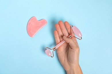 Photo of Woman with face roller and gua sha tool on light blue background, top view