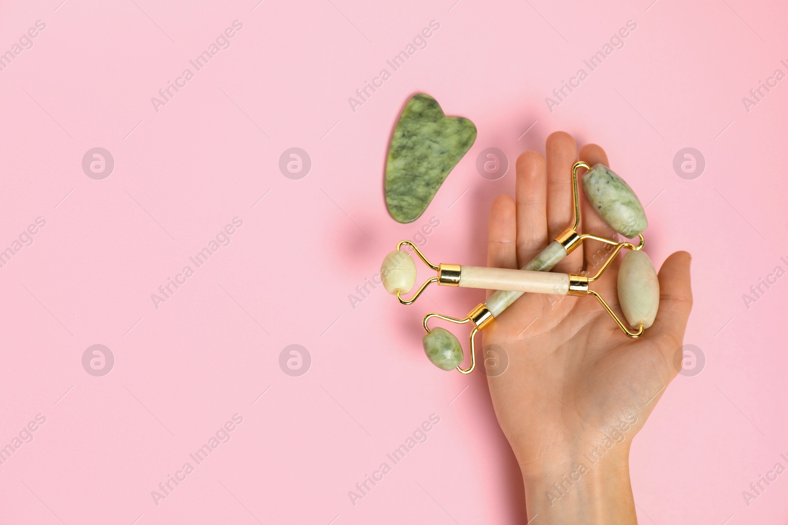 Photo of Woman with face rollers and gua sha tool on pink background, top view. Space for text