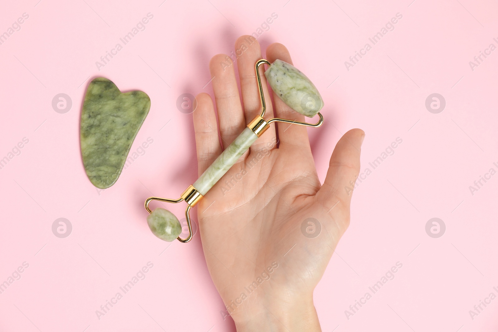 Photo of Woman with face roller and gua sha tool on pink background, top view