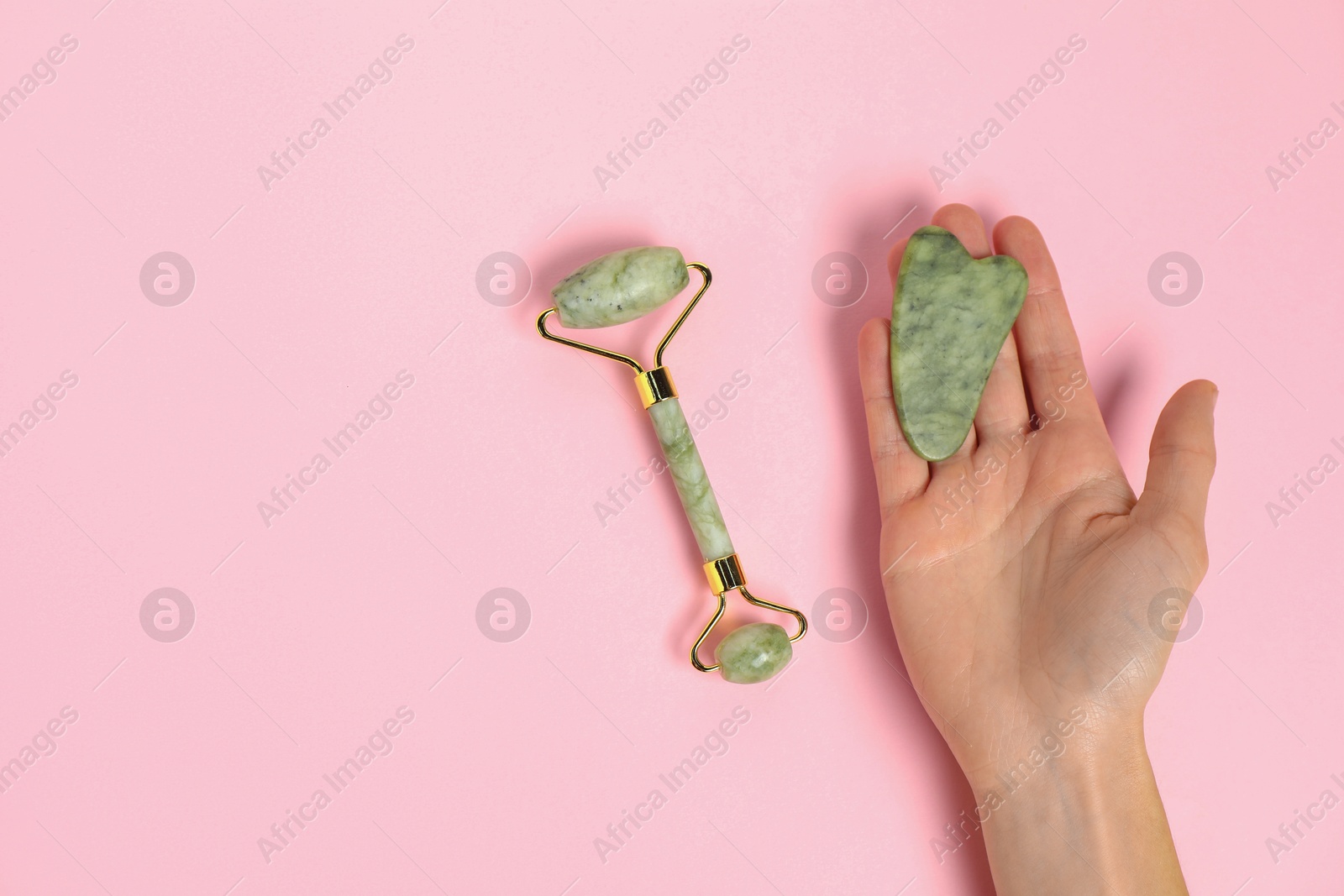 Photo of Woman with gua sha tool and face roller on pink background, top view. Space for text