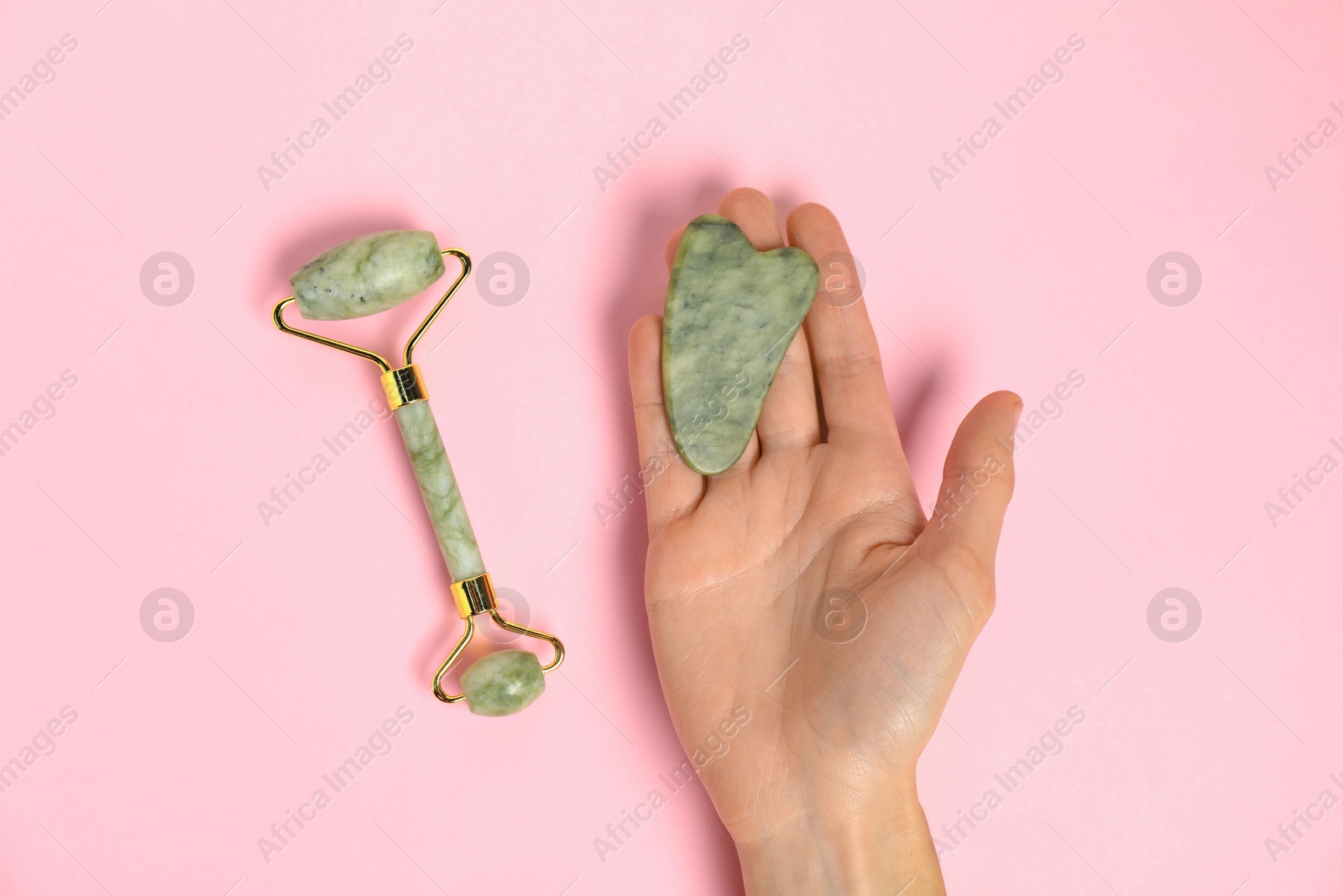 Photo of Woman with gua sha tool and face roller on pink background, top view