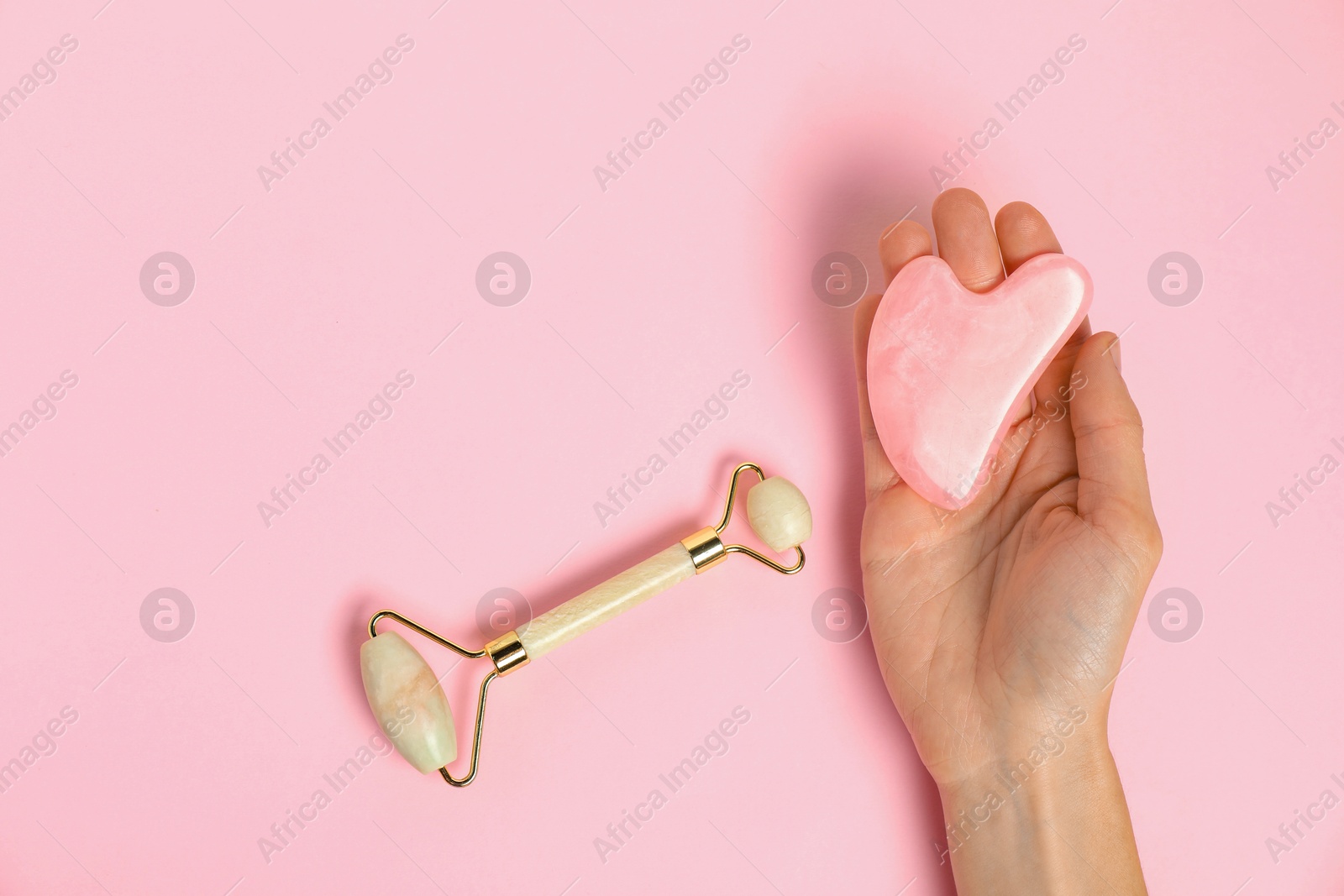 Photo of Woman with gua sha tool and face roller on pink background, top view