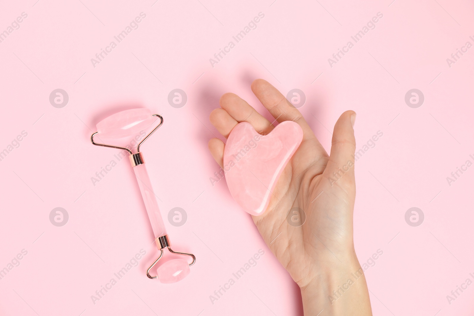 Photo of Woman with gua sha tool and face roller on pink background, top view