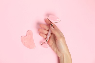 Photo of Woman with face roller and gua sha tool on pink background, top view