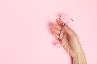 Photo of Woman with face roller on pink background, top view. Space for text