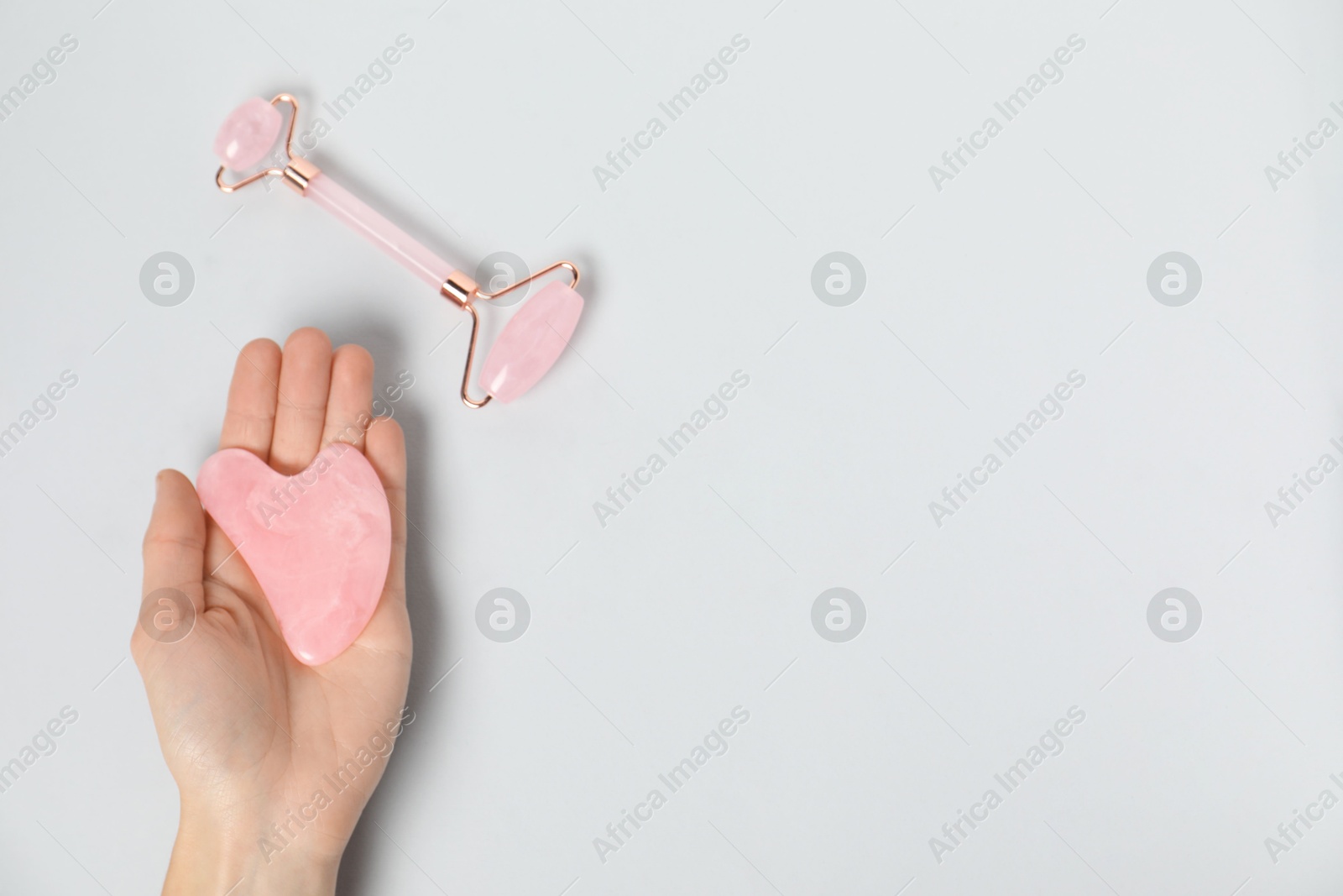 Photo of Woman with gua sha tool and face roller on light background, top view. Space for text