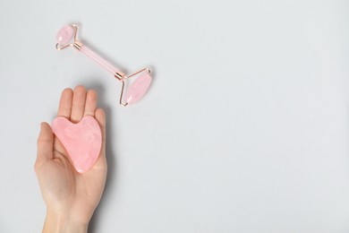 Photo of Woman with gua sha tool and face roller on light background, top view. Space for text