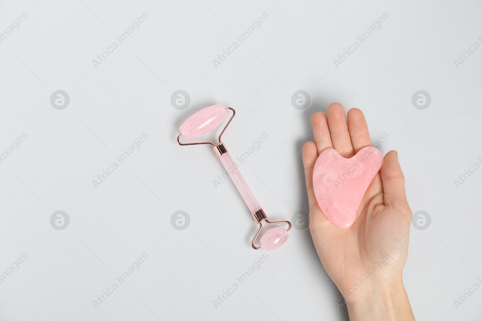 Photo of Woman with gua sha tool and face roller on light background, top view. Space for text