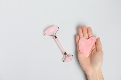 Photo of Woman with gua sha tool and face roller on light background, top view. Space for text