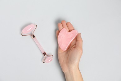 Photo of Woman with gua sha tool and face roller on light background, top view