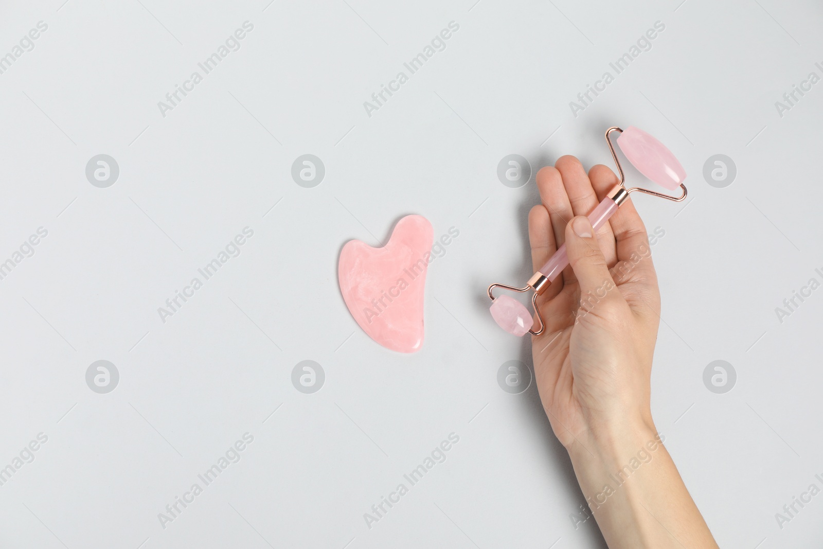 Photo of Woman with face roller and gua sha tool on light background, top view. Space for text