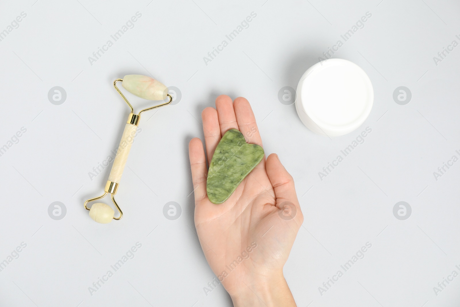 Photo of Woman with gua sha tool, face roller and cosmetic product on light background, top view