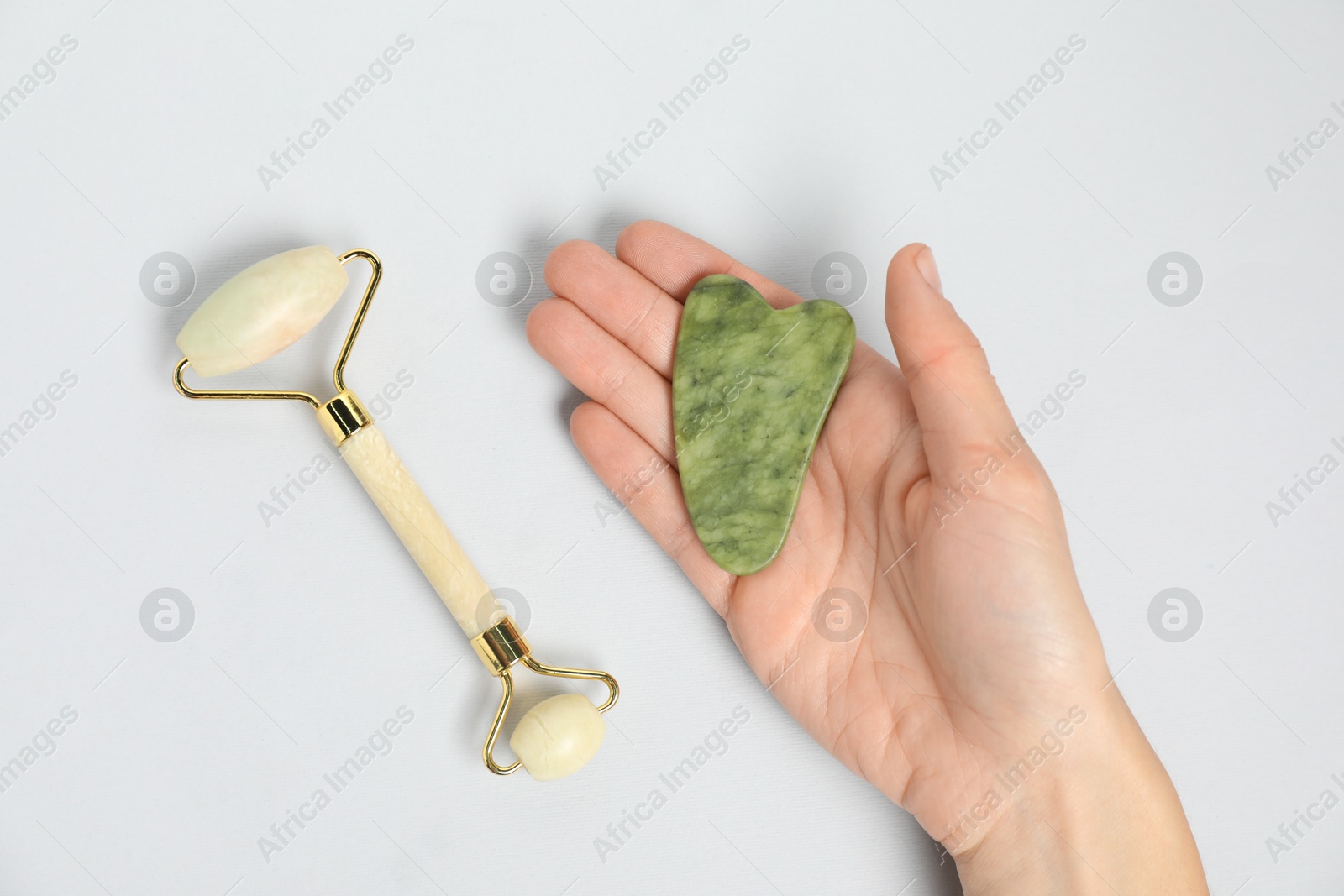 Photo of Woman with gua sha tool and face roller on light background, top view