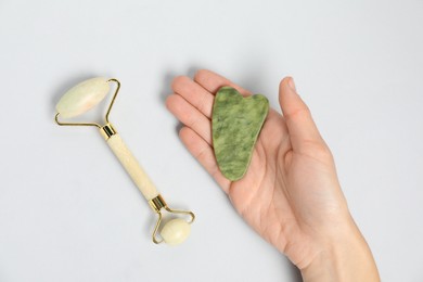 Photo of Woman with gua sha tool and face roller on light background, top view