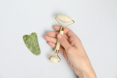 Photo of Woman with face roller and gua sha tool on light background, top view