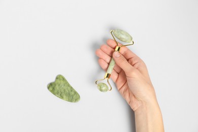 Photo of Woman with face roller and gua sha tool on light background, top view