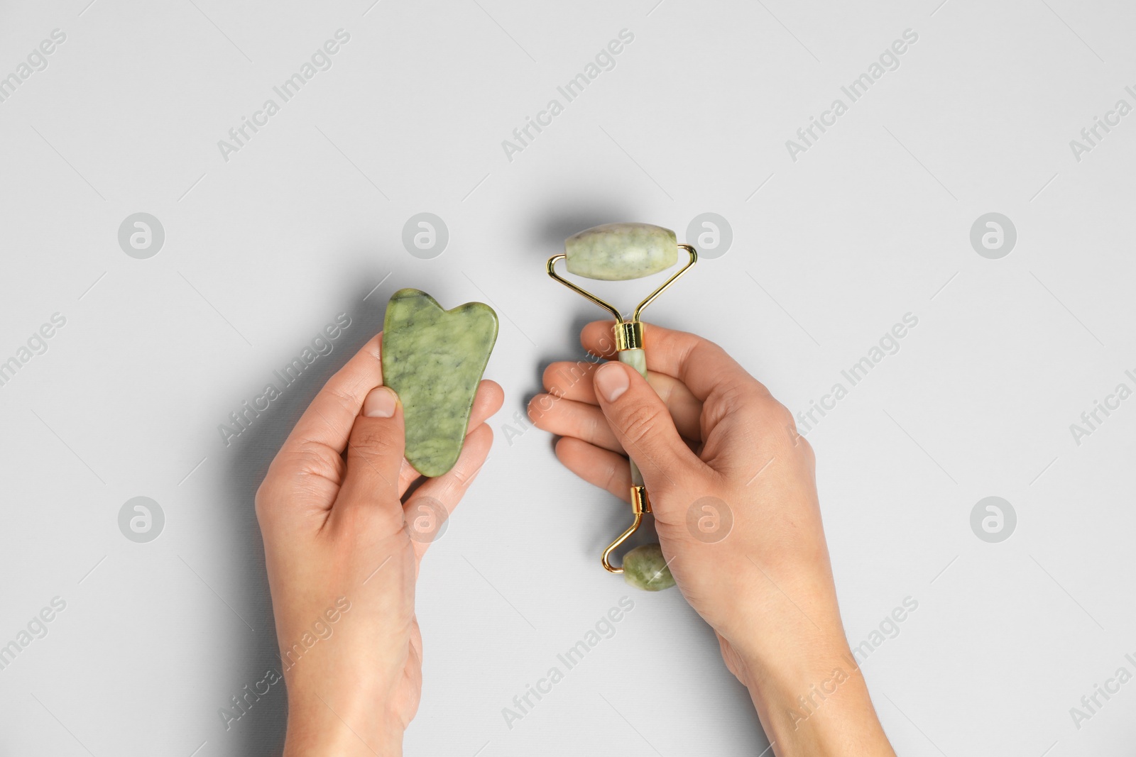 Photo of Woman with face roller and gua sha tool on light background, top view