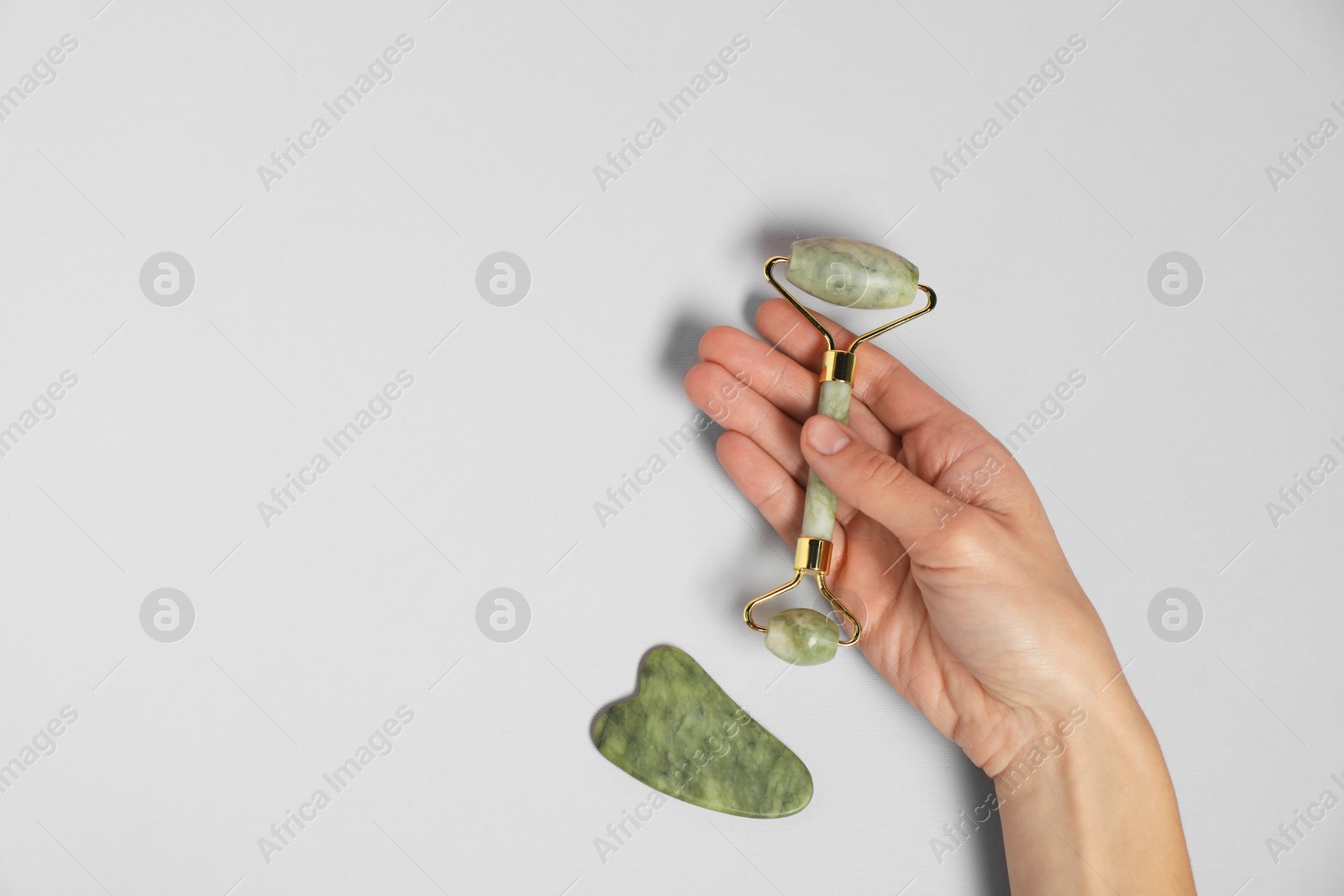 Photo of Woman with face roller and gua sha tool on light background, top view. Space for text