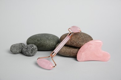 Photo of Face roller, gua sha tool and stones on light grey background