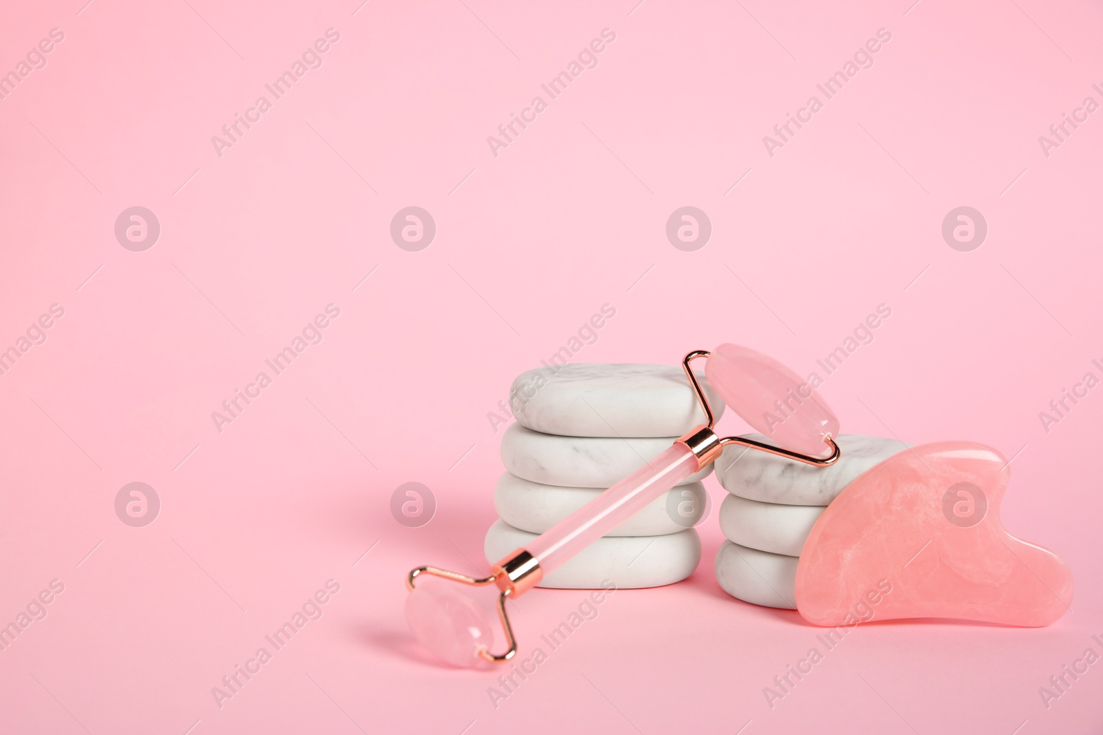 Photo of Face roller, gua sha tool and massage stones on pink background. Space for text