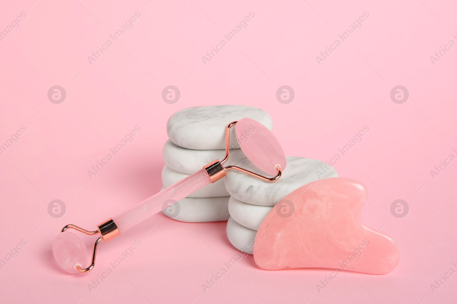 Photo of Face roller, gua sha tool and massage stones on pink background