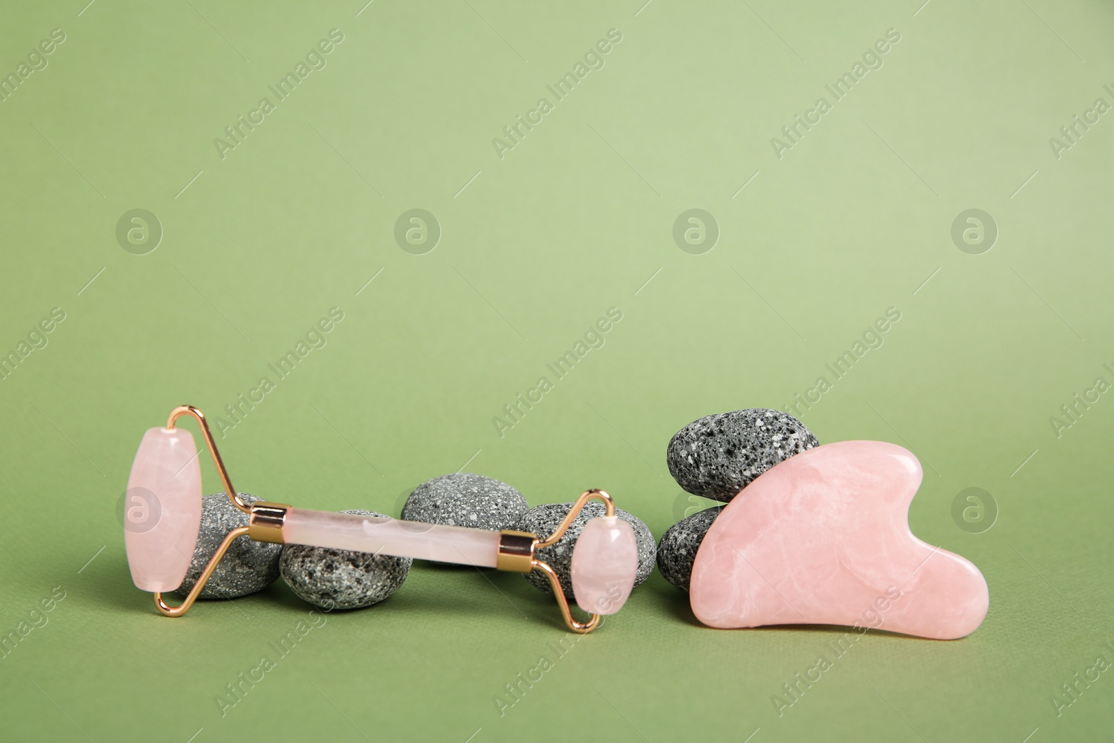 Photo of Face roller, gua sha tool and stones on green background. Space for text