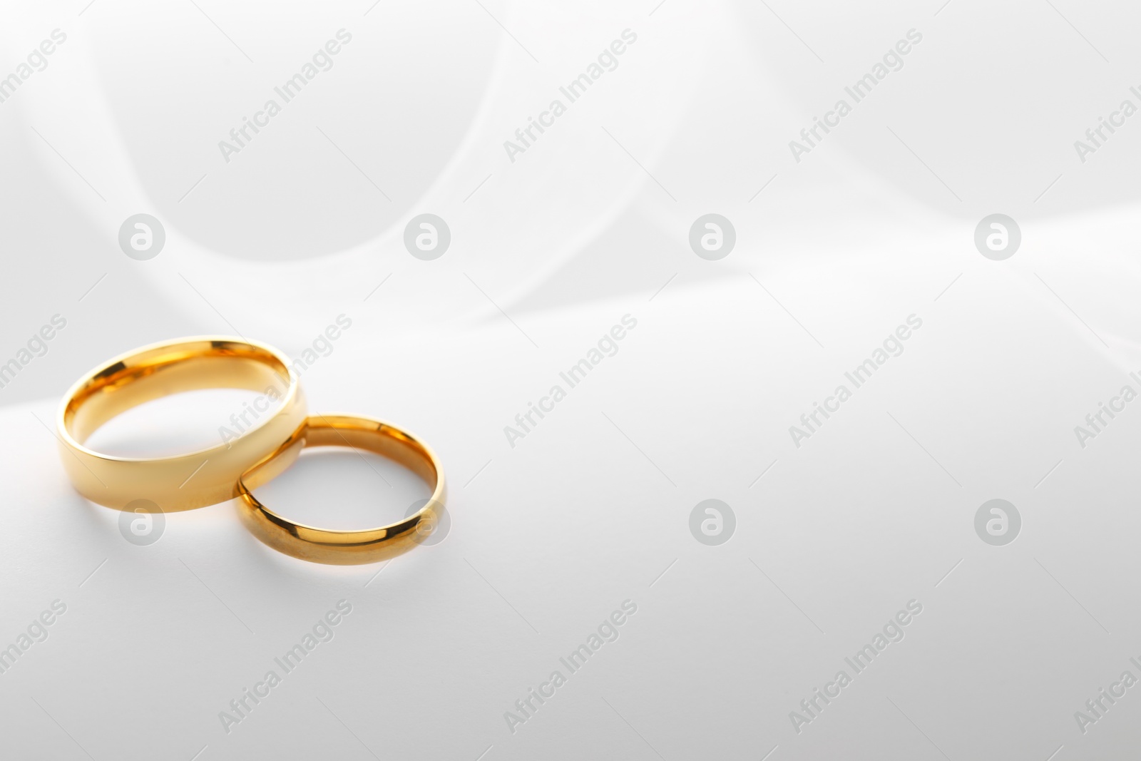 Photo of Beautiful golden wedding rings and white ribbon on light background