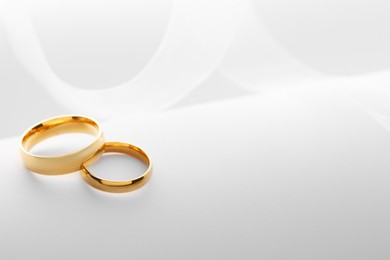 Beautiful golden wedding rings and white ribbon on light background