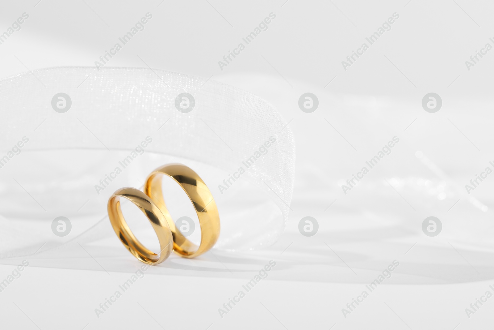 Photo of Beautiful golden wedding rings and ribbon on white background