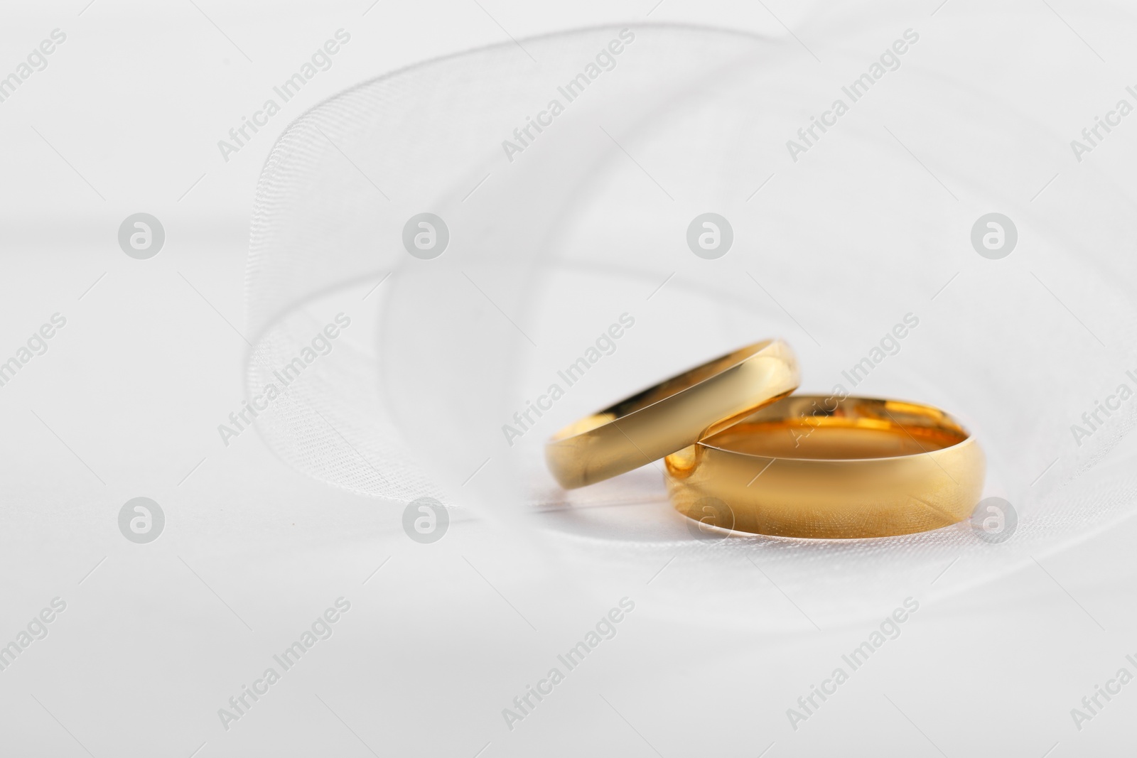 Photo of Beautiful golden wedding rings and ribbon on white background, closeup